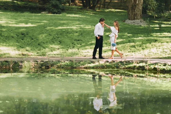 Bräutigam küsst Braut Hand, die in der Nähe des Sees im Park steht — Stockfoto