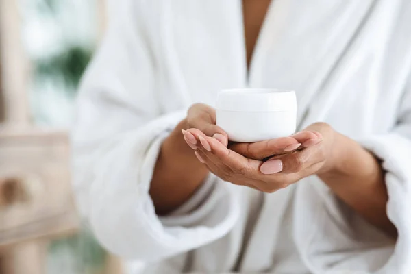 Glas mit nährender Creme in den Händen einer nicht wiedererkennbaren schwarzen Frau im Bademantel — Stockfoto