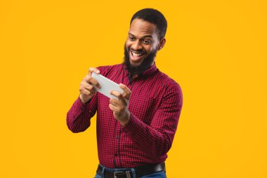 Sarı arka planda cep telefonu kullanan heyecanlı afro adam.