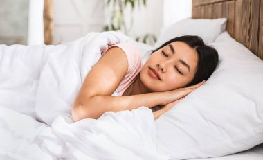 Asyalı kız yatakta iyi uyuyor. Evde dinleniyor.