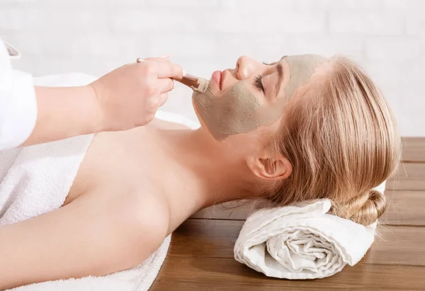 Anti-aging face mask. Beautician applied clay on skin of girl lying on table in spa salon — Stock Photo, Image