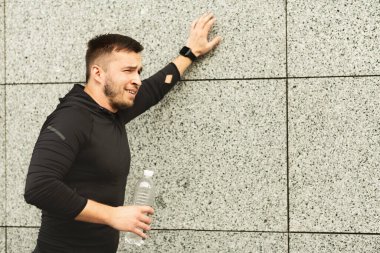 Yorgun bir adam uzun bir koşudan sonra duvara yaslanıyor.