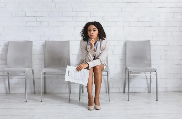 Weary young lady with CV waiting for screening interview at office lobby. Copy space