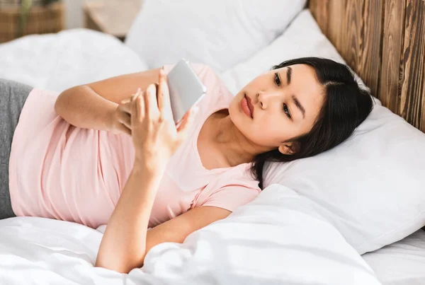 Femme chinoise utilisant Smartphone allongé dans le lit à la maison, Angle élevé — Photo