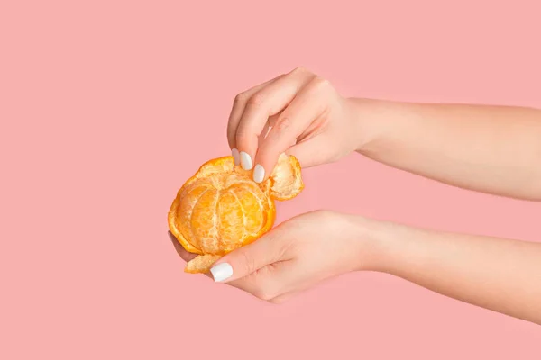 Menina milenar descascando fruta laranja fresca no fundo rosa, close-up de mãos — Fotografia de Stock