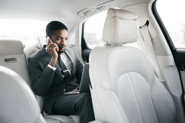 Empresário sério trabalhando no portátil, falando no telefone celular no carro — Fotografia de Stock