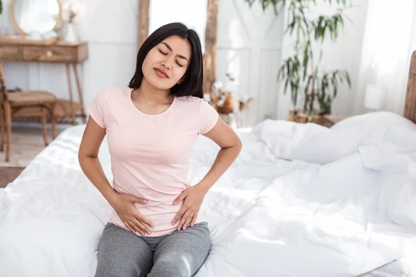 Азиатка, имеющая трогательный желудок страдает от менструальных спазмов в помещении — стоковое фото