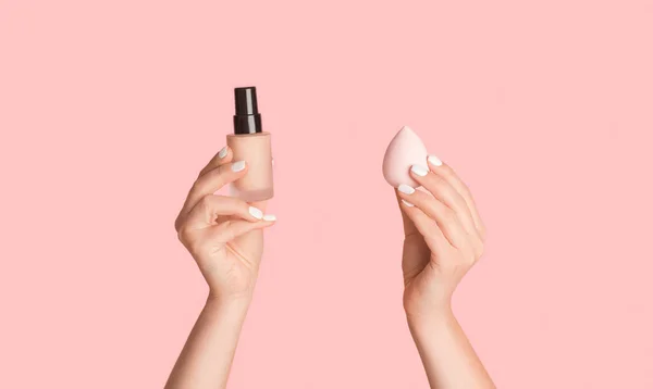 Close-up van vrouwelijke handen tonen fles van cosmetische foundation en spons op roze achtergrond, panorama — Stockfoto