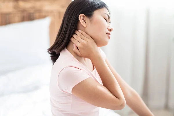 Asiática mujer masaje aguijón cuello sentado en cama en casa — Foto de Stock