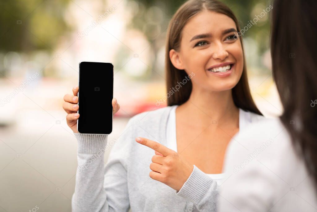 Girl Showing Smartphone Blank Screen To A Friend Walking Outside