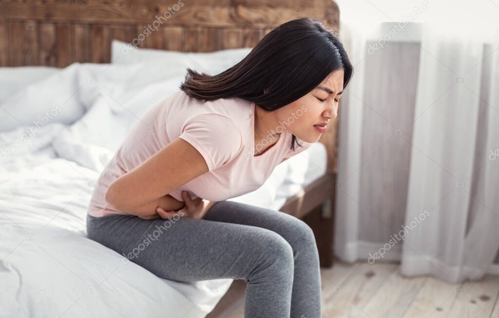 Asian Girl Having Abdominal Pain Sitting In Bed At Home