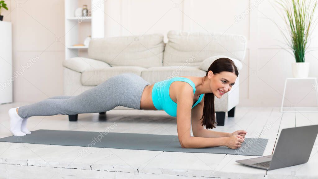 Young Woman At Laptop Exercising Doing Plank During Home Workout