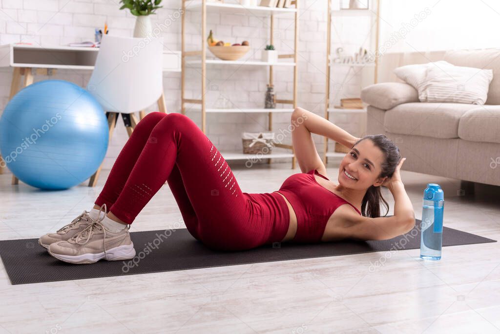 Stay home, stay active. Attractive young woman doing abdominal crunches on yoga mat indoors