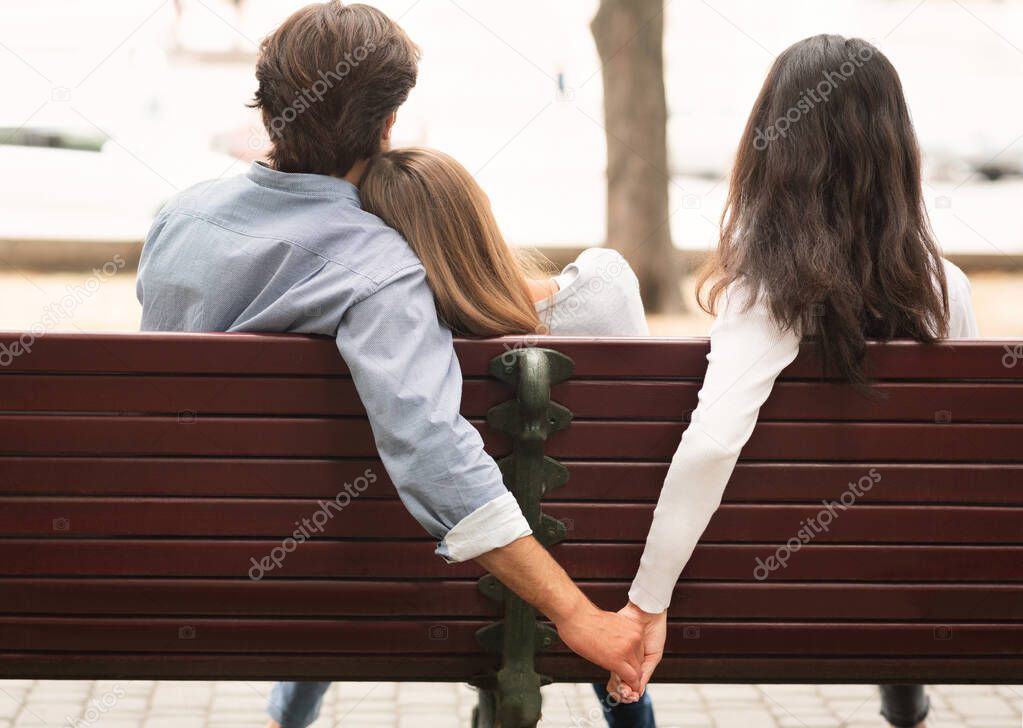 Boyfriend Holding Hands With Girlfriends Friend Sitting On Bench Outdoor