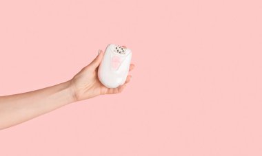 Tanımlanamayan bir kız pembe arka planda modern elektrikli epilatör tutuyor, yakın plan. Uzayı kopyala Panorama