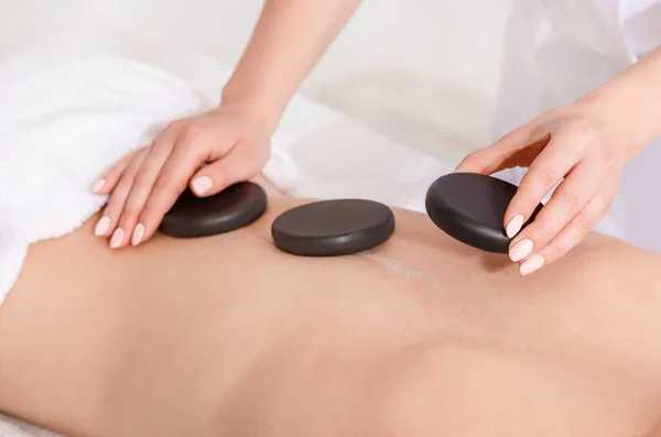 Spabehandlingar för skönhet. Händerna lägger heta stenar på kvinnan tillbaka på massagebordet — Stockfoto
