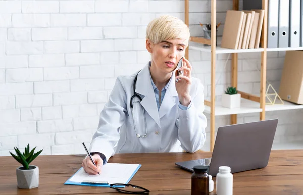 Appointment with doctor. Woman speaks on smartphone and looks at laptop — Stock Photo, Image