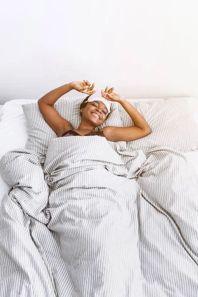 Sonriente chica afroamericana en la máscara del sueño despertó en el dormitorio —  Fotos de Stock