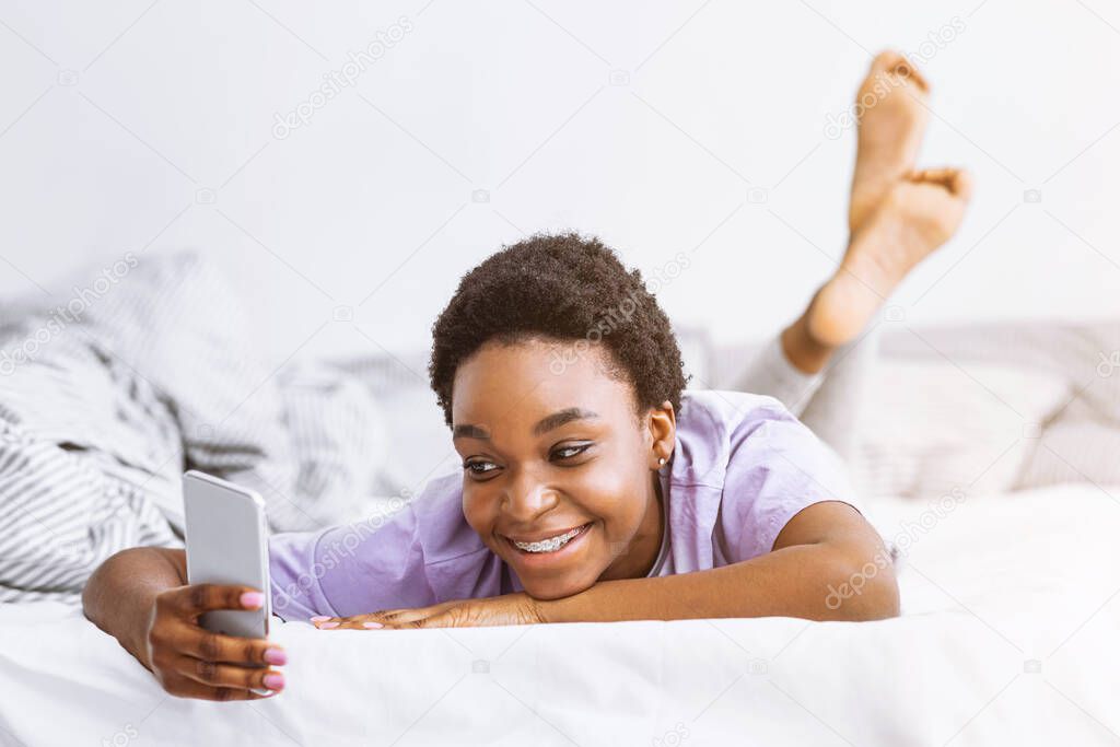 Smiling african american girl looking and typing on smartphone
