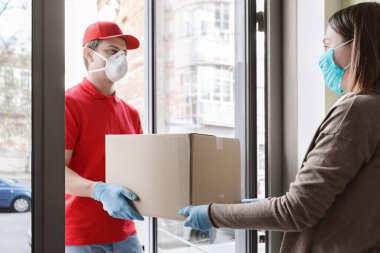 Koruyucu maskeli ve eldivenli kurye kendini izole eden kıza paket veriyor.