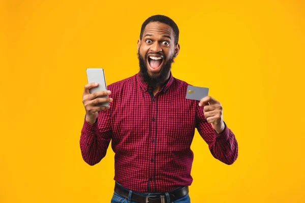 Homem negro segurando cartão de crédito e celular no estúdio — Fotografia de Stock