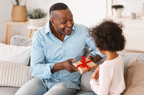A legjobb szülinapi ajándék. Az idős afro-amerikai férfi ajándékot ad otthon a göndör lánynak. — Stock Fotó