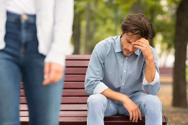 Неузнаваемая девушка оставляет грустного парня сидеть на скамейке запасных в парке — стоковое фото