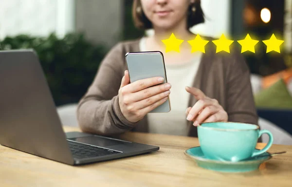 Mujer sosteniendo el teléfono y mirando en la pantalla, dando cinco estrellas para la encuesta — Foto de Stock