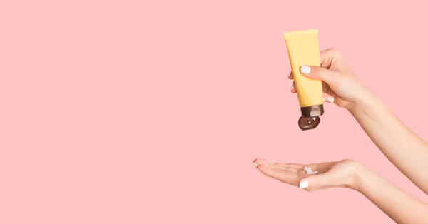 Gros plan de jeune femelle appliquant de la crème pour les mains sur fond rose, espace de copie. Panorama — Photo