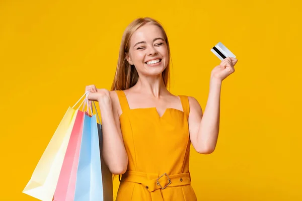 Glada flicka med shoppingväskor och kreditkort över gul bakgrund — Stockfoto