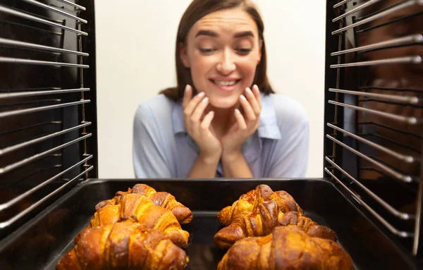 Radostná dívka při pohledu na chutné čerstvé croissanty v troubě — Stock fotografie
