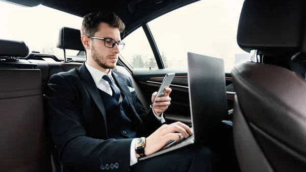 Pengusaha yang duduk di mobil mewah menggunakan telepon dan pc — Stok Foto