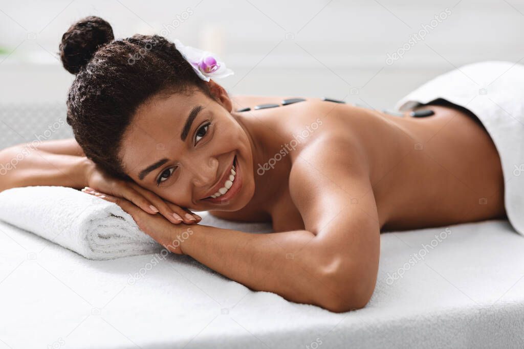 Cheerful black woman in spa salon with hot stones