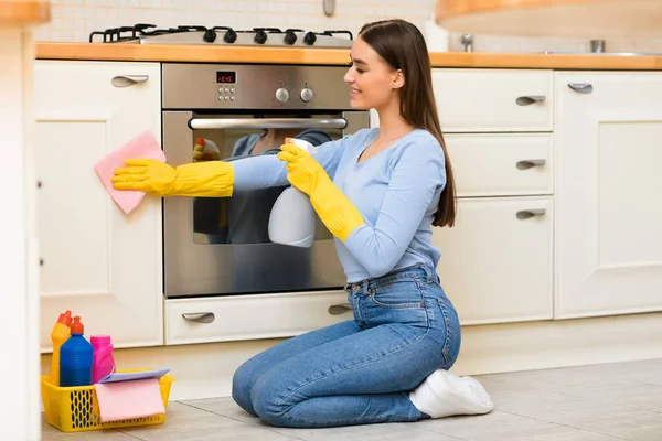 Jovem mulher limpeza de móveis de cozinha usando pulverizador — Fotografia de Stock