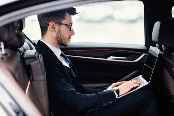 Młody biznesmen korzystający z laptopa w luksusowym samochodzie — Zdjęcie stockowe