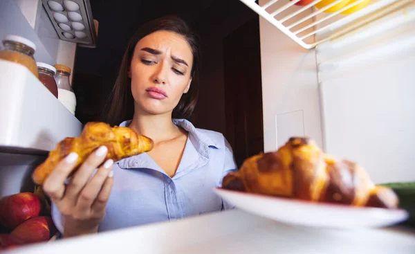 Zamyšlená dívka se dívá na croissant s pochybnostmi — Stock fotografie