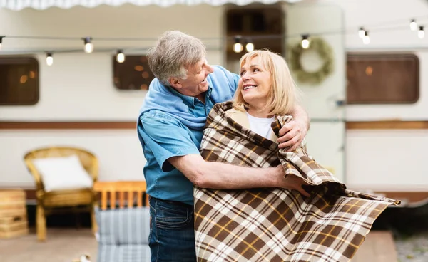 Happy senior man putting plaid on his beloved wifes shoulders at camping site — Stock Photo, Image