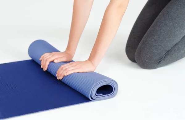 Close-up van jonge vrouw rollen haar yoga mat op witte achtergrond — Stockfoto