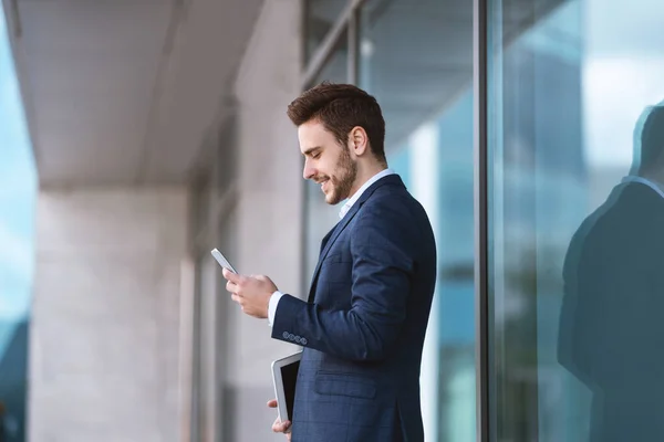 Joven emprendedor confiado utilizando su teléfono móvil para la comunicación en línea cerca del centro de negocios — Foto de Stock