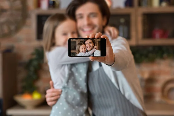 Happy dad and daughter taking selfie on smartphone while cooking at kitchen