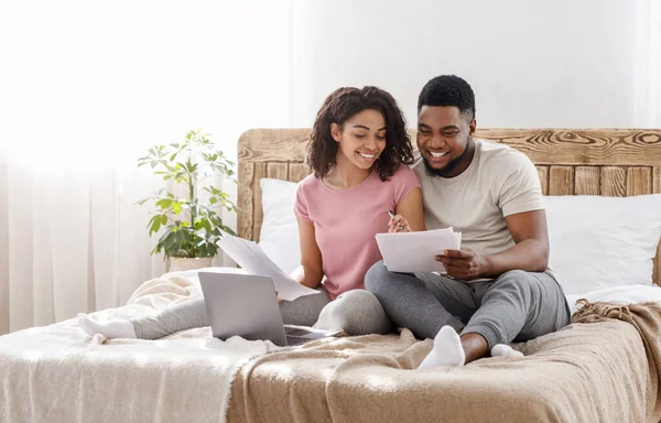 Νεαρό μαύρο ζευγάρι κάθεται στο κρεβάτι στο σπίτι, τον έλεγχο του προϋπολογισμού — Φωτογραφία Αρχείου