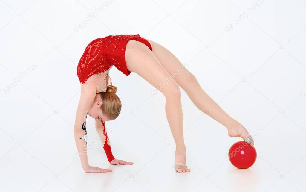 Flexible rhythmic gymnast with ball doing backbend on white background