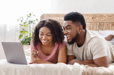 Yatakta dizüstü bilgisayar kullanan komik Afrikalı çift.