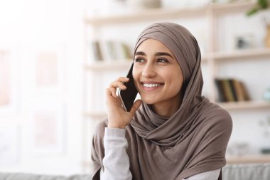 Modern İletişim. tesettürlü gülümseyen Arap kadın evde cep telefonuyla konuşuyor.