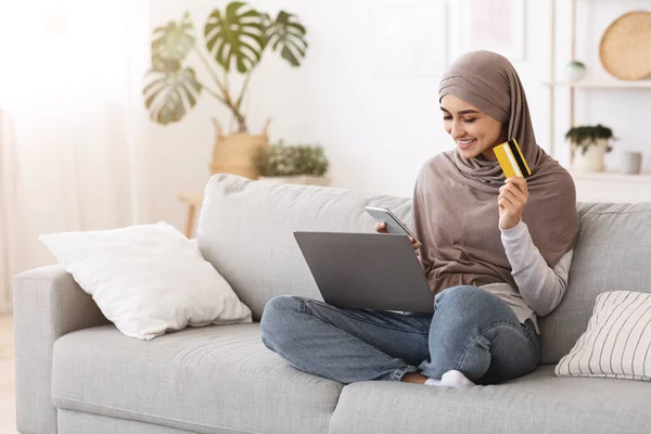 Compras en línea. Mujer musulmana usando smartphone, laptop y tarjeta de crédito en casa — Foto de Stock
