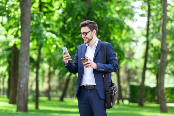 Attractive business executive with takeaway coffee browsing internet in green park — Stock Photo, Image