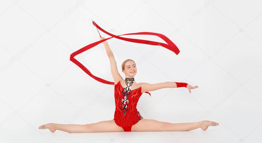 Professional gymnast with red ribbon doing leg split on white background, panorama