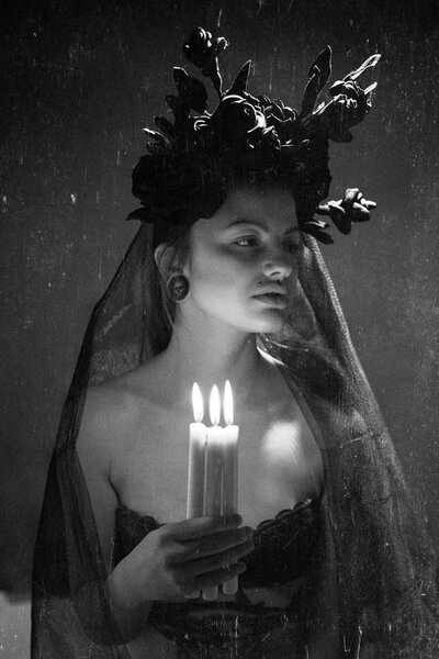Black and white portrait of beautiful young woman with black flowers and veil holding candles