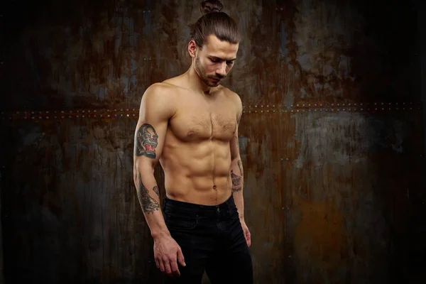 Handsome young shirtless tattooed man posing against grunge background