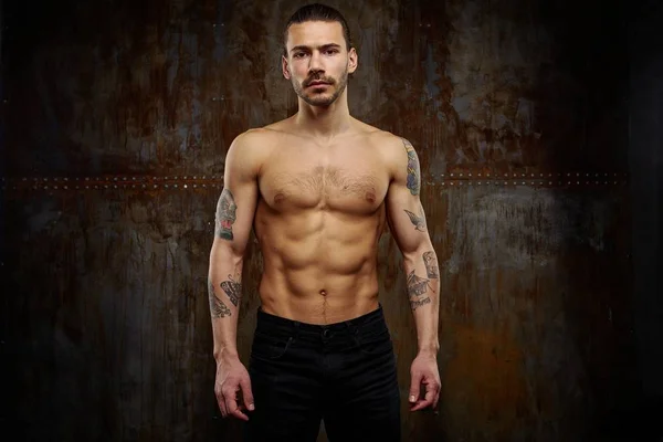 Handsome young shirtless tattooed man posing against grunge background